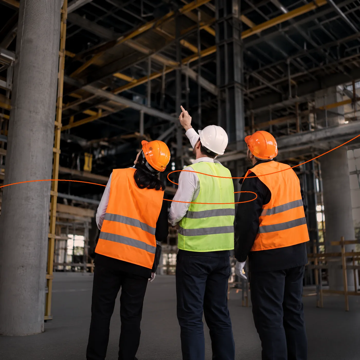Three workers in hard hats and high-visibility vests looking up at the steel frame of a building under construction